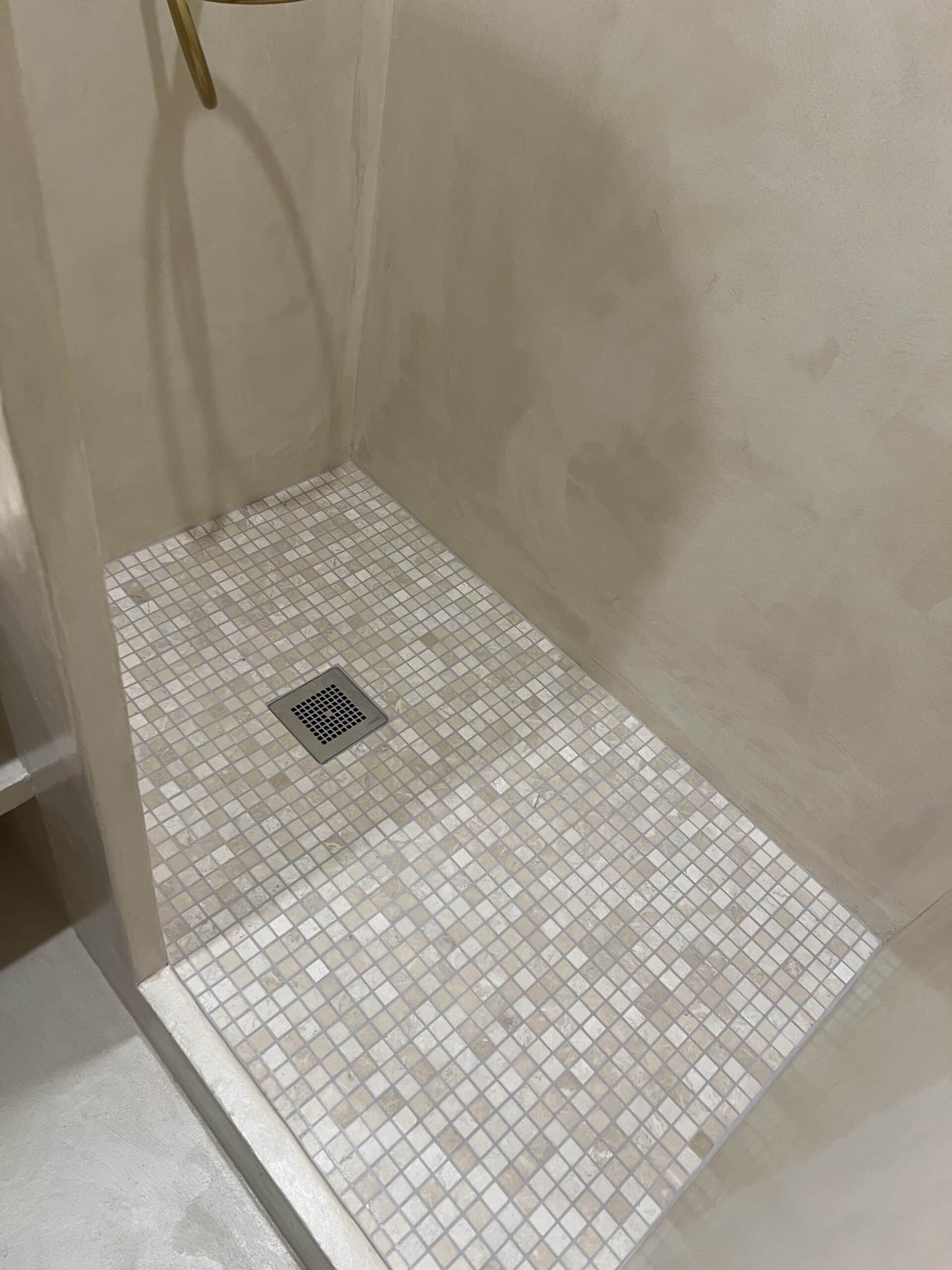Sol de douche en mosaïque de pierre naturelle beige à Nantes, bonde carrée et murs en béton ciré
