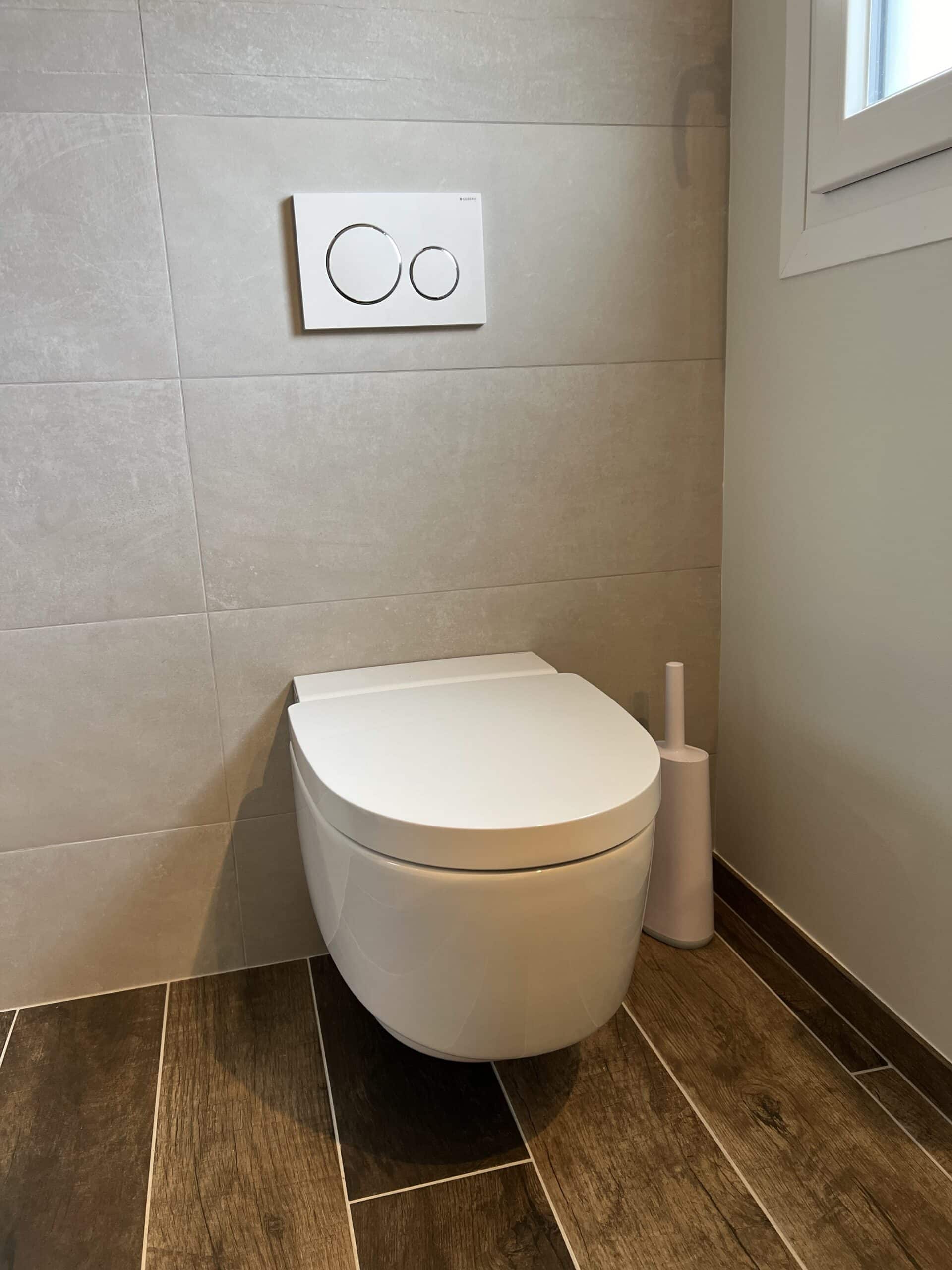 WC suspendu Geberit à Saint-Herblain, plaque de commande ronde chromée, carrelage gris clair et sol imitation bois