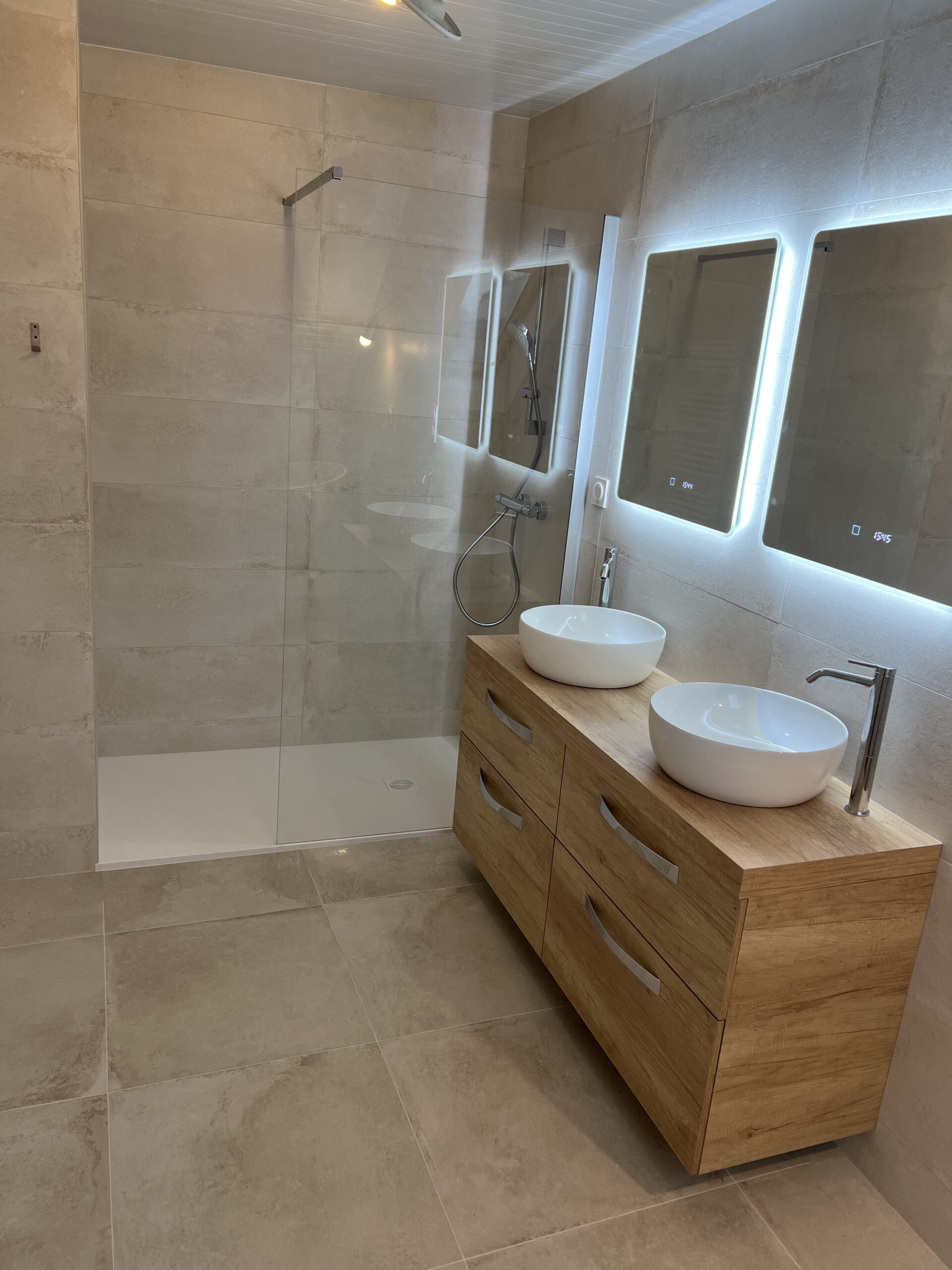 Rénovation salle de bain La-Chapelle-Sur-Erdre — vue ensemble douche italienne receveur extra-plat, double vasque à poser sur meuble chêne et triple miroirs rétroéclairés LED, grès cérame grand format effet travertin